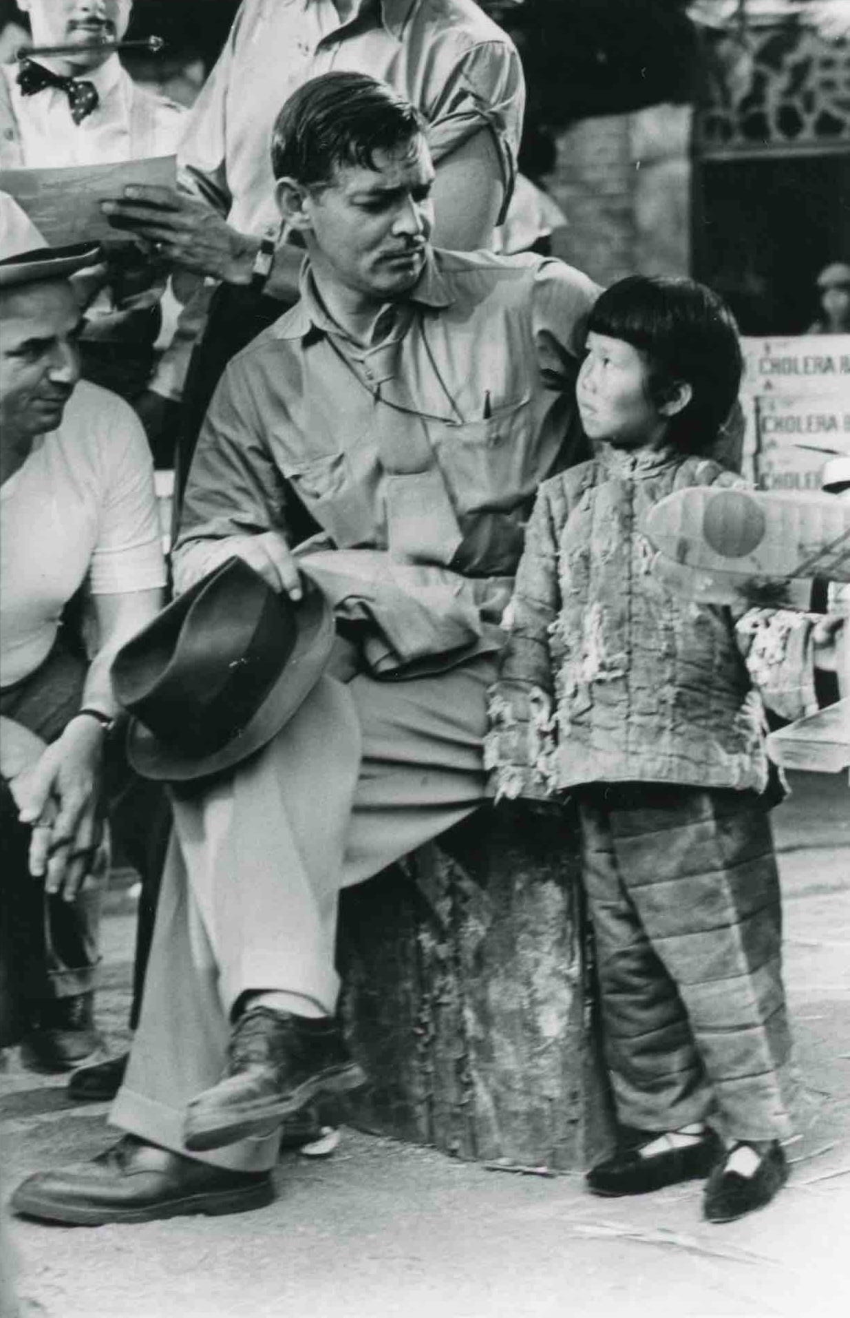 black and white photo of a little Chinese girl standing next to Clark Gable on film set