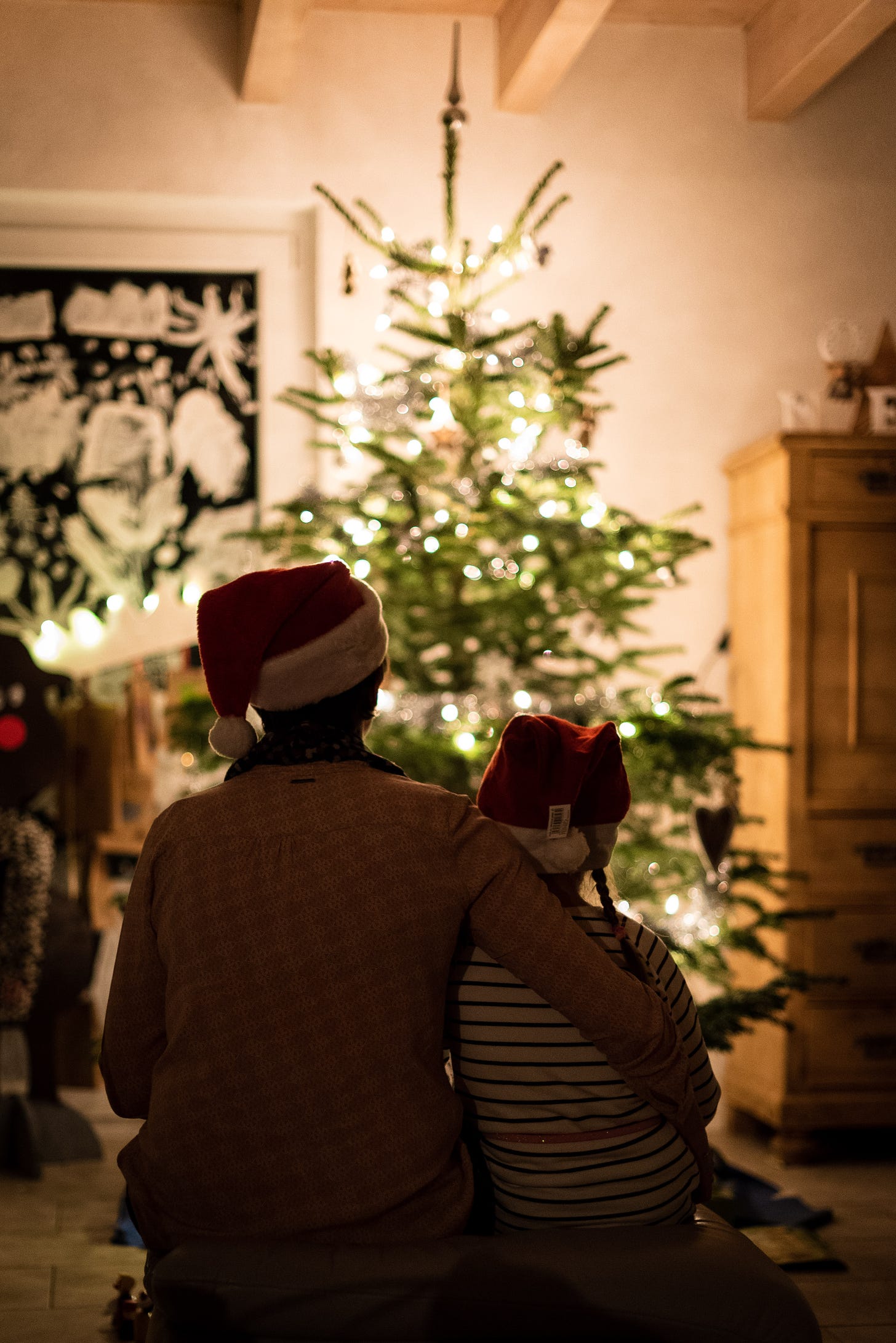 Father and daughter wearing Santa caps sitting in front of a Christmas tree