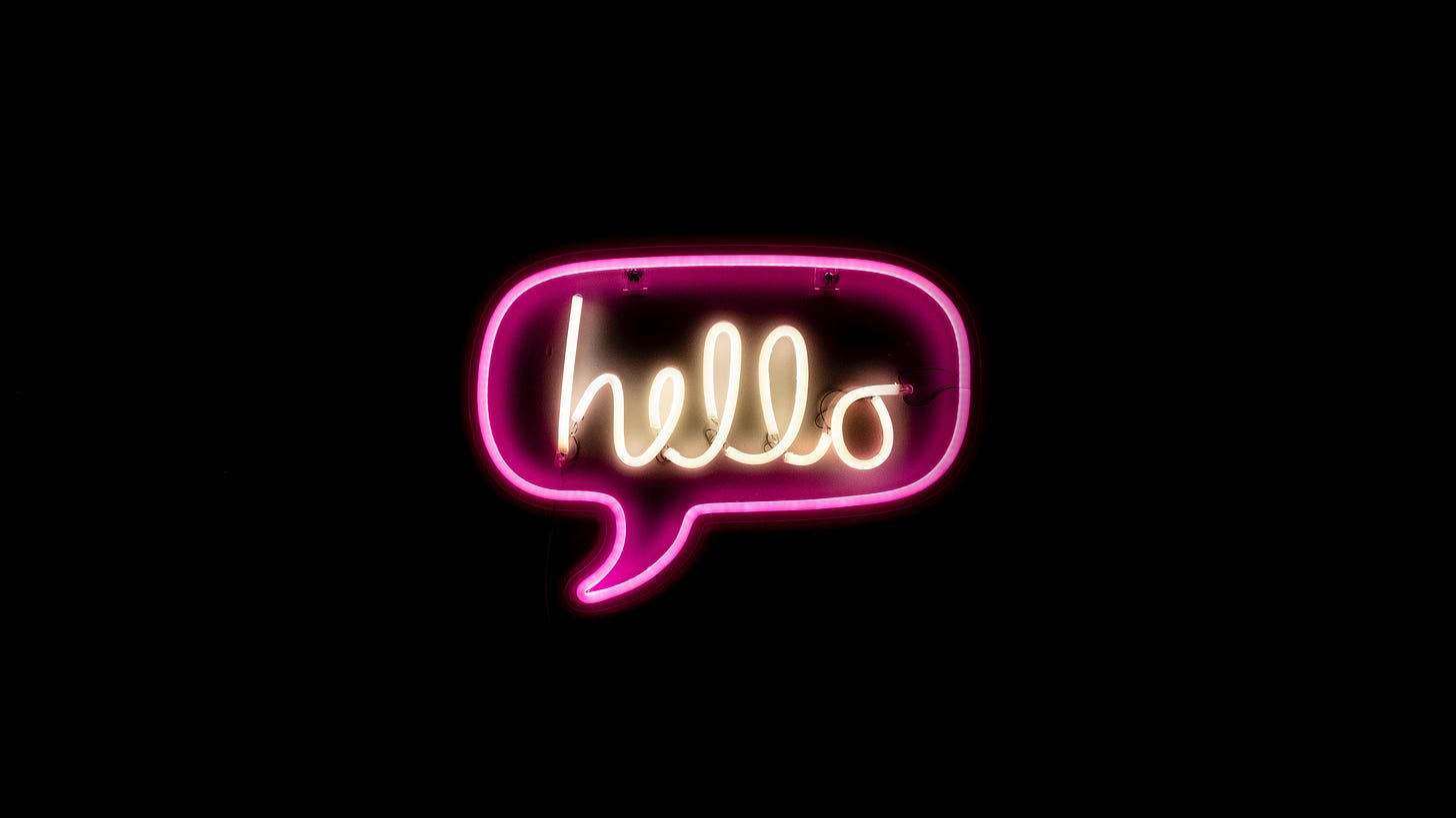 A photo of a pink and white neon "hello" sign on a black background.