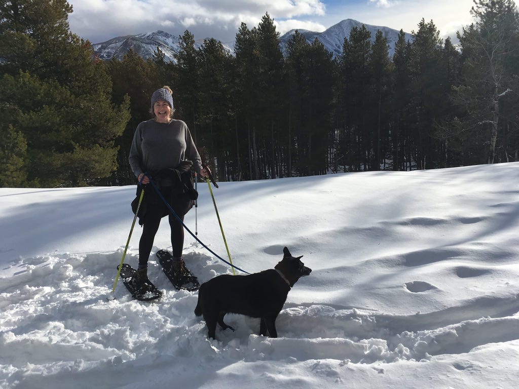 Woman and black dog snowshoeing in the mountains.