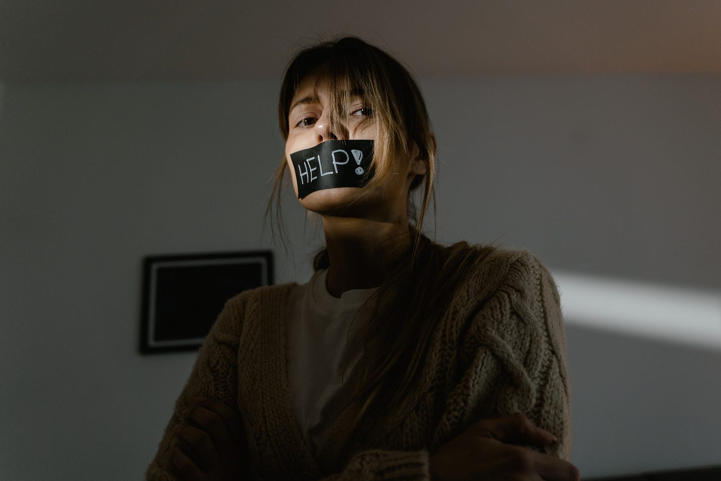 a person in a dark room with back tape on their mouth that says help in white