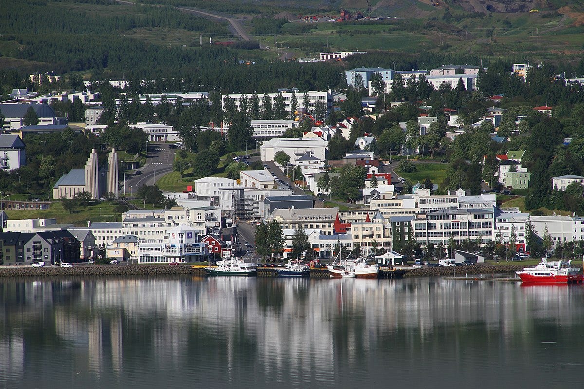 Photo of Akureyri, a picturesque Icelandic town on a mountainside by the sea. It looks clean and modern, with light-coloured buidlings, plenty of trees, and some boats.