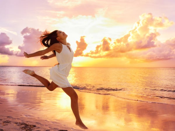 A woman in a short white dress running happily along the shore as the sun sets behind her