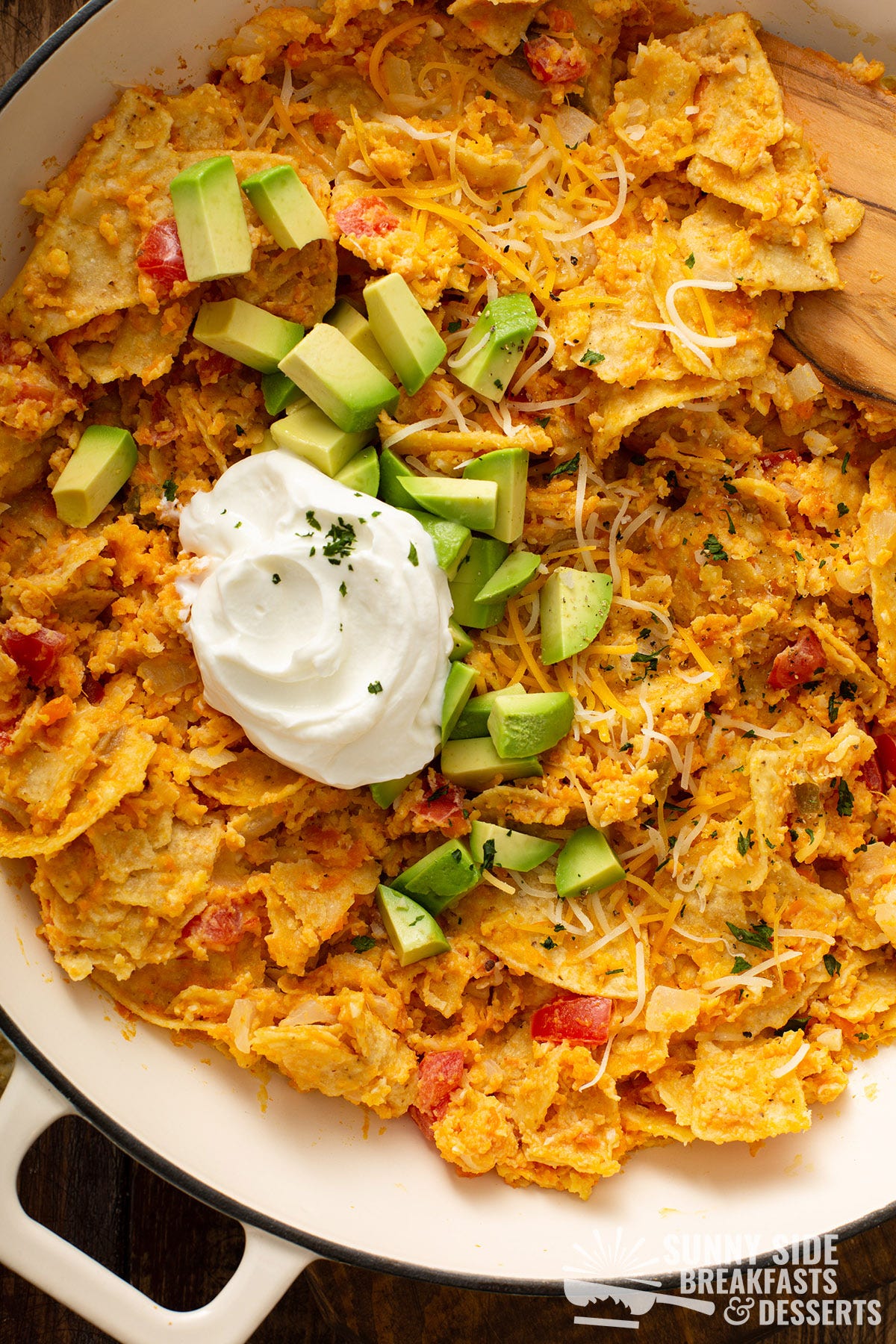 Sweet potato migas in a pan topped with sour cream and diced avocado.