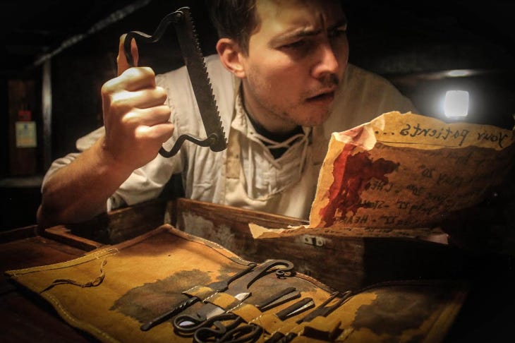 An actor examining a list of patients while holding old-fashioned surgical tools