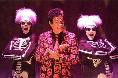 a man in an orange suit pointing to two flanking skeletons