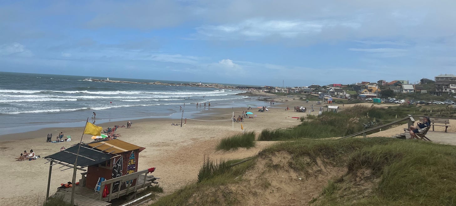 a calm beach with lifeguard station and people sitting in the sand in Punta del Diablo