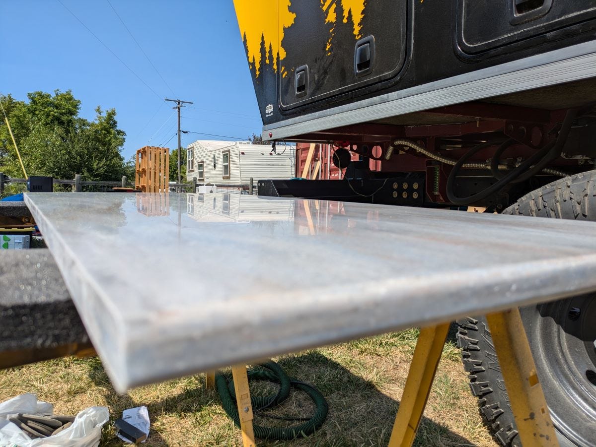 A shiny slab of countertop reflecting the camper and the structures beyond it like a mirror