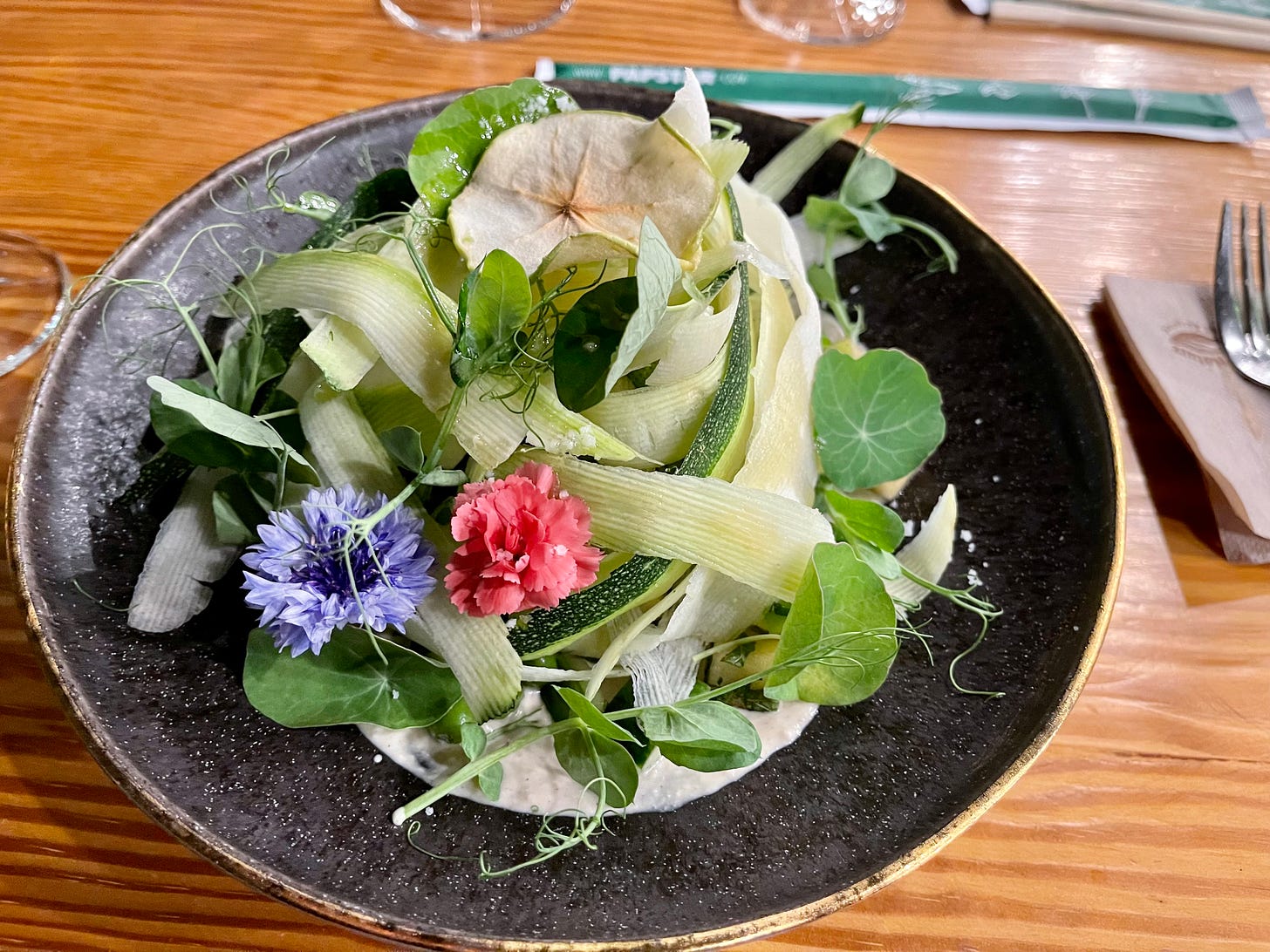 Salad with apple, zucchini and flower decorations on a black plate