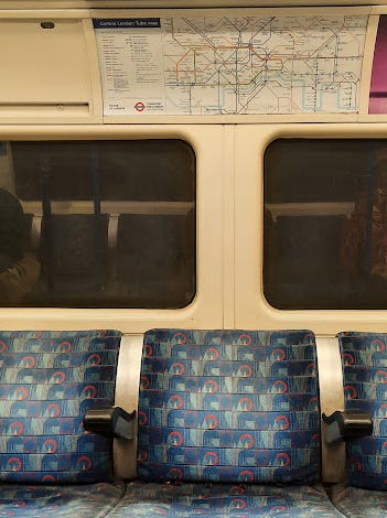 Empty seats on the London Tube. The fabric is faded and the windows are black.
