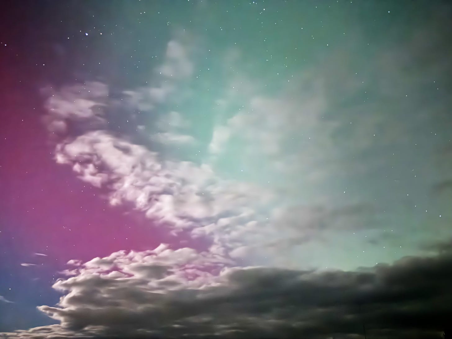 Aurora behind night-sky clouds appears pink, lavender, and an unusual bottle green.