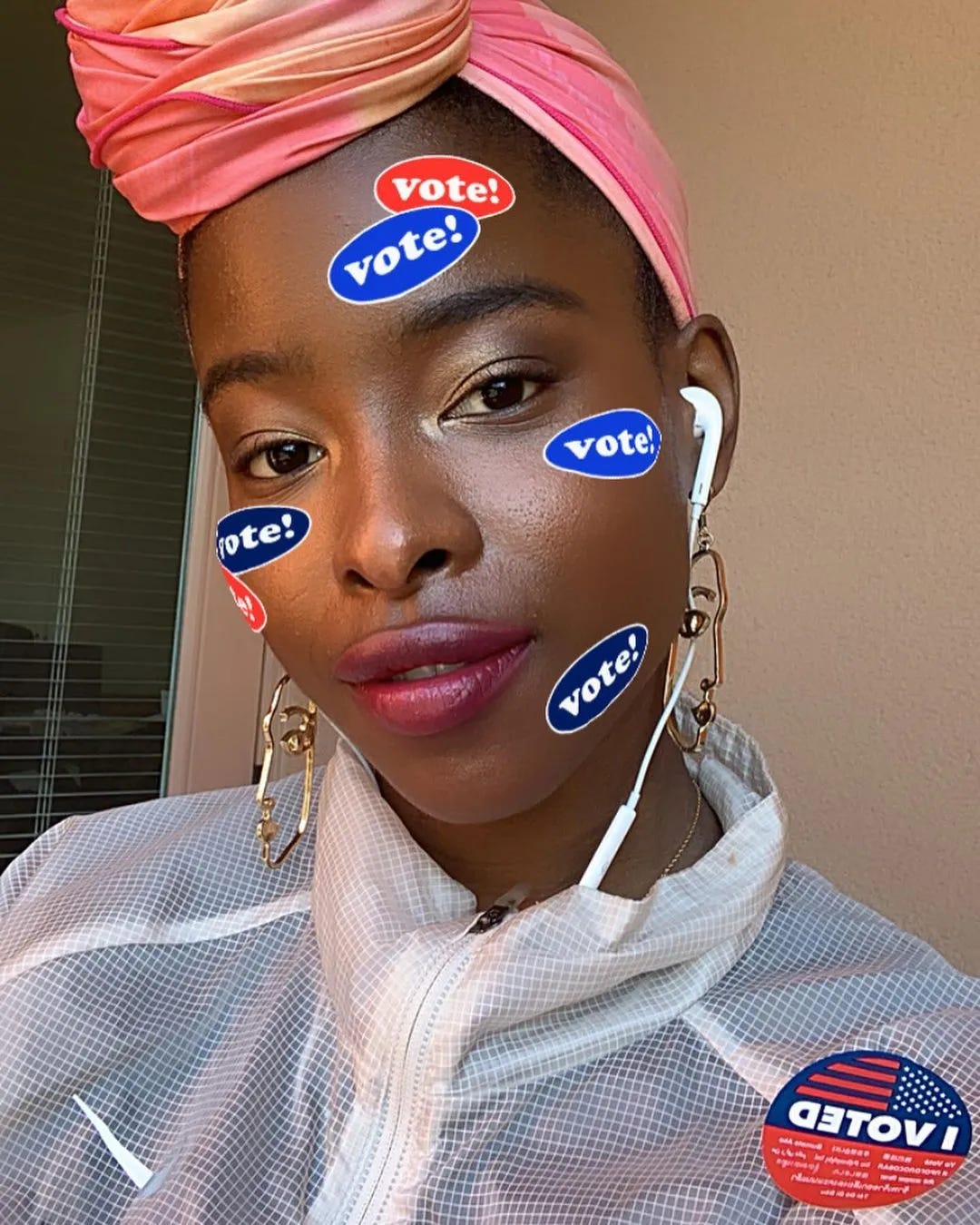 Head and shoulders photo of a young woman with "Vote!" stickers on her face. The high color of a white jacket sets off her dark skin.