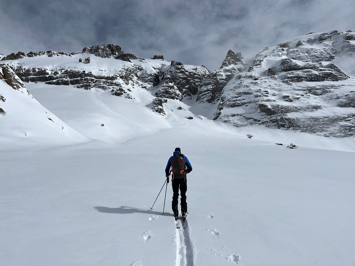 A man skiing uphill into snow covered mountains