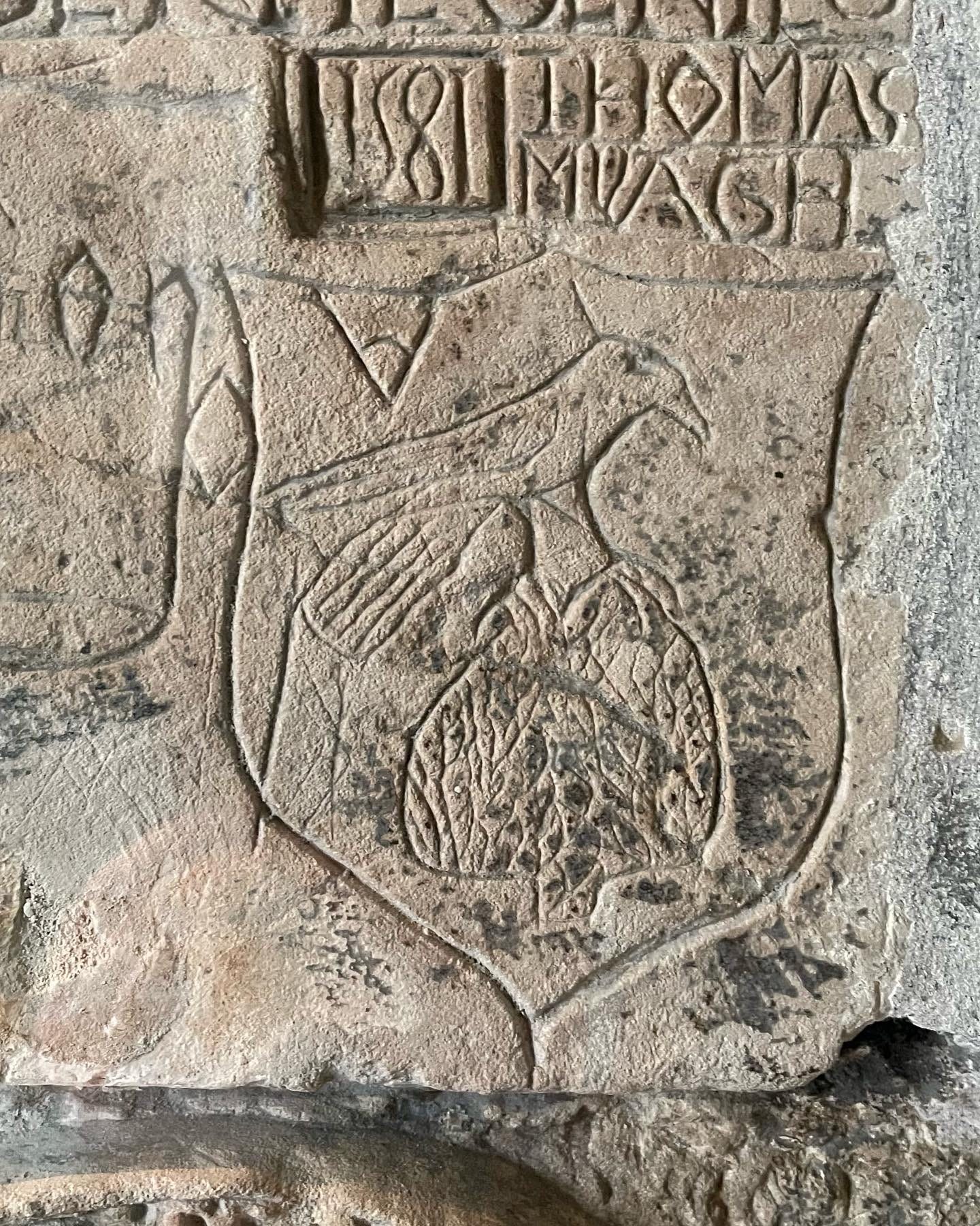 A carving in stone of a crude falcon within a shield shape