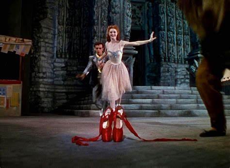 Una scena del film Scarpette rosse (1948). in primo piano un paio di scarpette da danza rosse, sullo sfondo il palco di un teatro con la scenografia di una vecchia chiesa e una ballerina dai capelli rossi che sta andando verso le scarpette.
