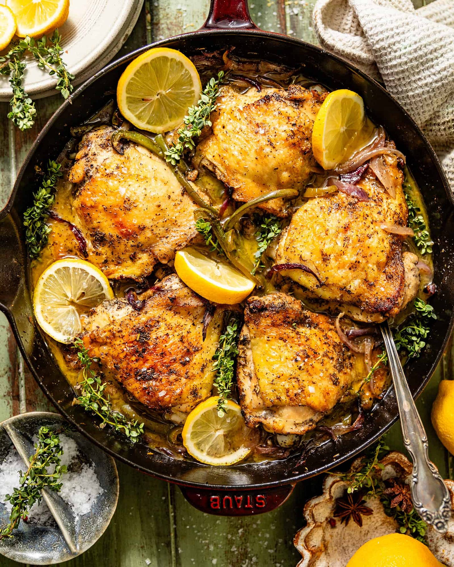 an overhead photo of chicken thighs in a skillet with a serving spoon.
