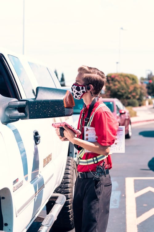 Free Fast food employee interacts with customers at a drive-thru, wearing mask and uniform for safety. Stock Photo