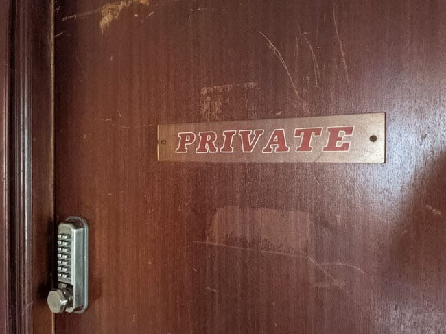 A plastic sign on a battered door that reads "Private".