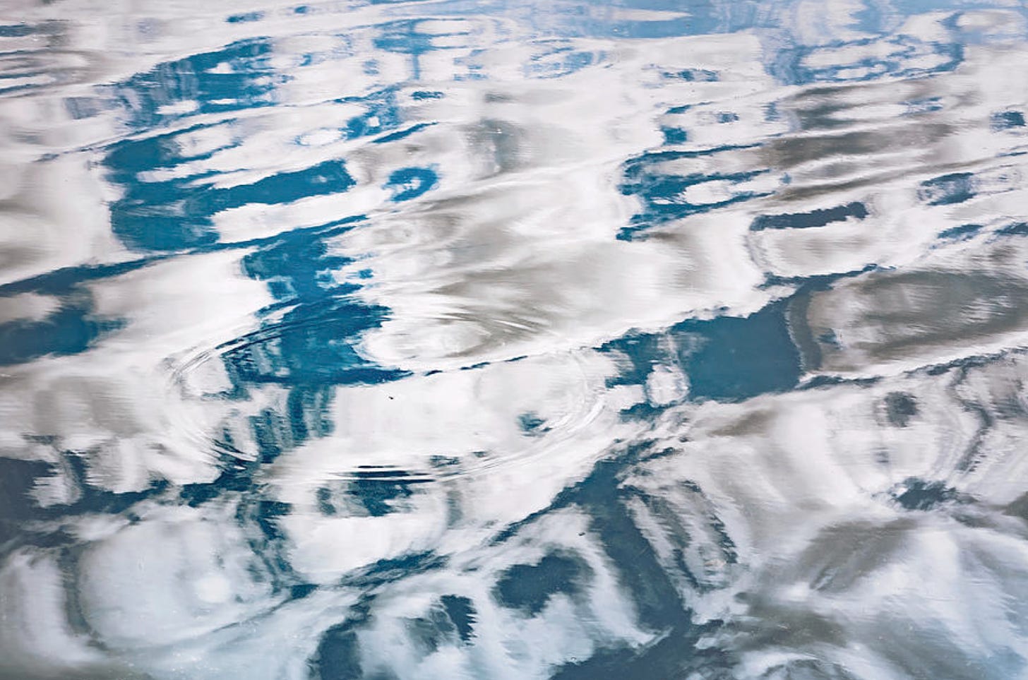 Surface of a pond with ripples and reflections of clouds.