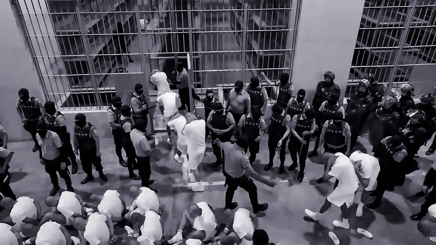 Image of Prisoners rounded up to be prepared for insertion into their 80–200-person cell/cage by CECOT officers/thugs. Most prisoners have their heads bowed unnaturally in a state of subservience.