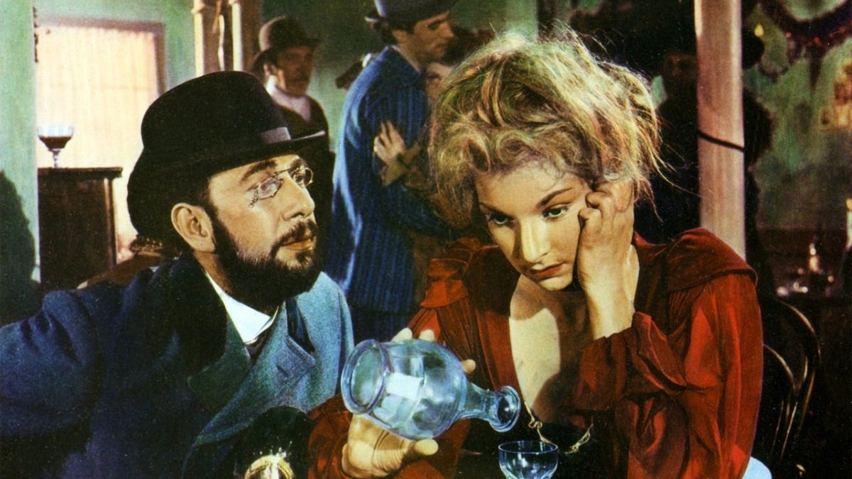 José Ferrer as Henri de Toulouse-Lautrec and Colette Marchand as Marie Charlet in Moulin Rouge. She appears tired and stares into space as she pours alcohol into a glass while he looks at her hopefully