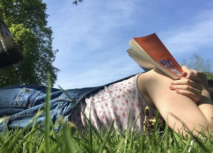 This may contain: a person laying in the grass reading a book