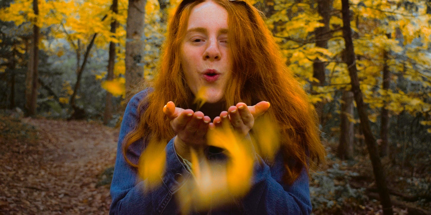 woman blowing leaves in autumn forest