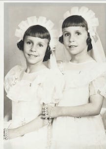 Image shows twin girls in white dresses and white headbands, holding rosaries