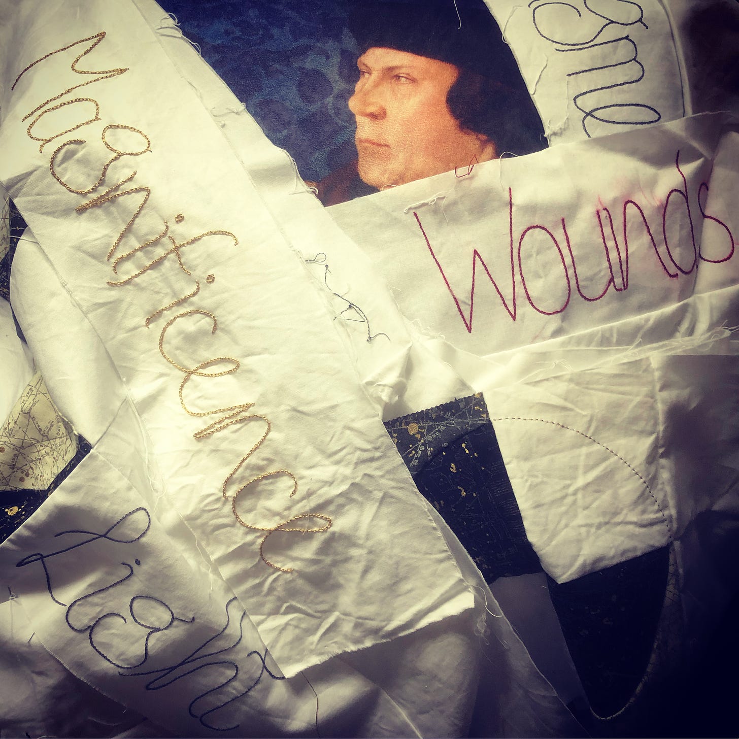 Stitched words on strips of light coloured fabric are piled on top of a cushion featuring the face of Thomas Cromwell