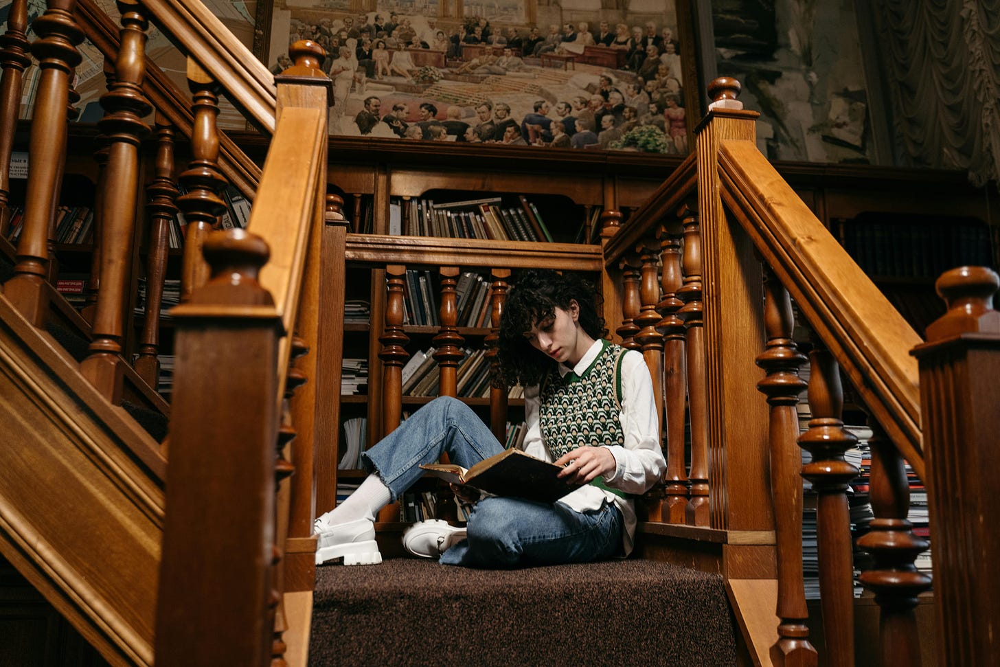 College student sitting on library stairs reading a book