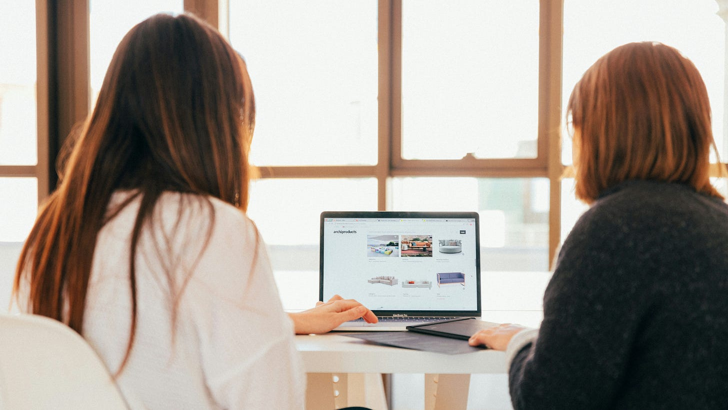 Two women collaborating while browsing a product website on a laptop in a bright, modern office space, symbolizing teamwork and creative decision-making. Two women collaborating while browsing a product website on a laptop in a bright, modern office space, symbolizing teamwork and creative decision-making.
