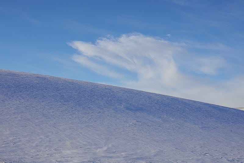 Powder snow drifts across of a snow covered field under blue Aberdeenshire sky