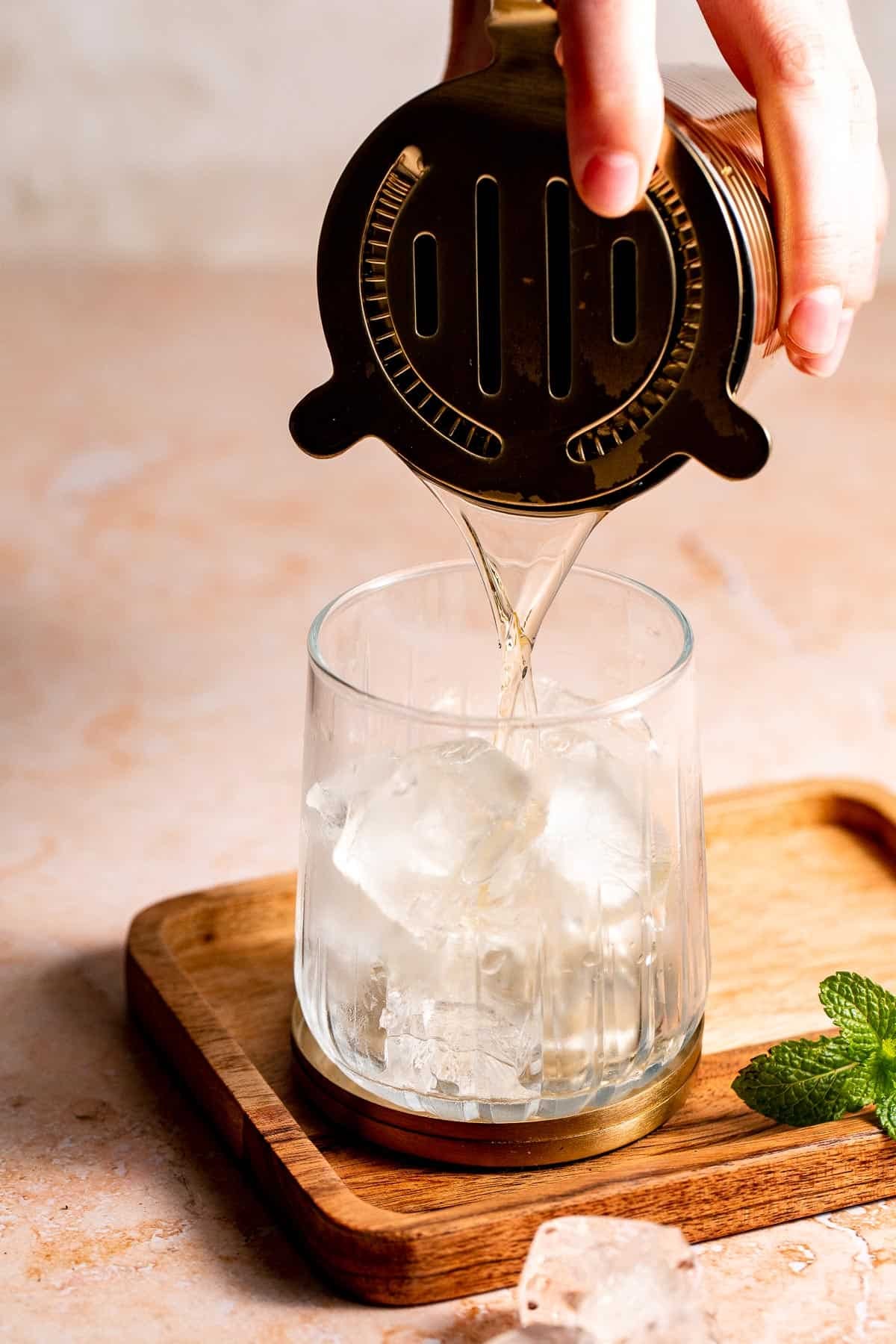 A cocktail being strained into a serving glass filled with ice