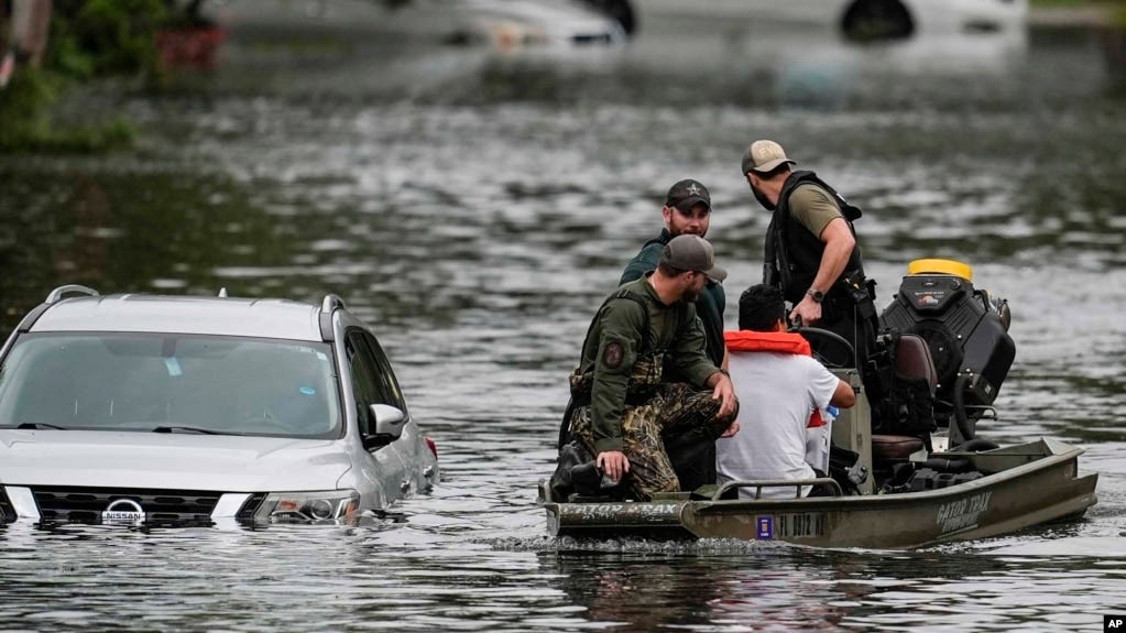 Emergency responders rescue a man in a flood on a small raft. A submerged car is beside them.