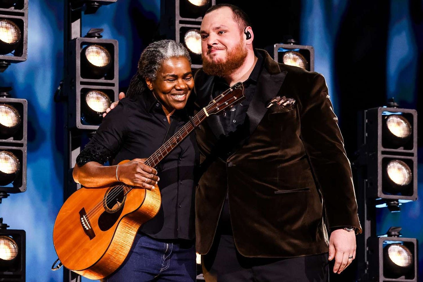 Image of Tracy Chapman holding her guitar, smiling and hugging an also emotional Luke Combs on stage at the 2024 Grammys
