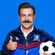 picture of Jason Sudekis as Ted Lasso holding a soccer ball under one arm and giving a thumbs up with the other