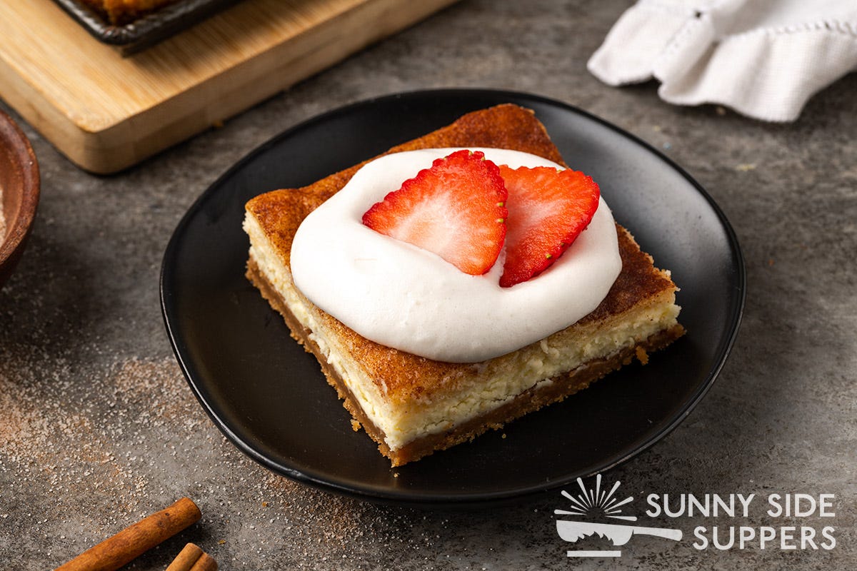 Slice of churro cheesecake with whipped cream and strawberry slices on top.