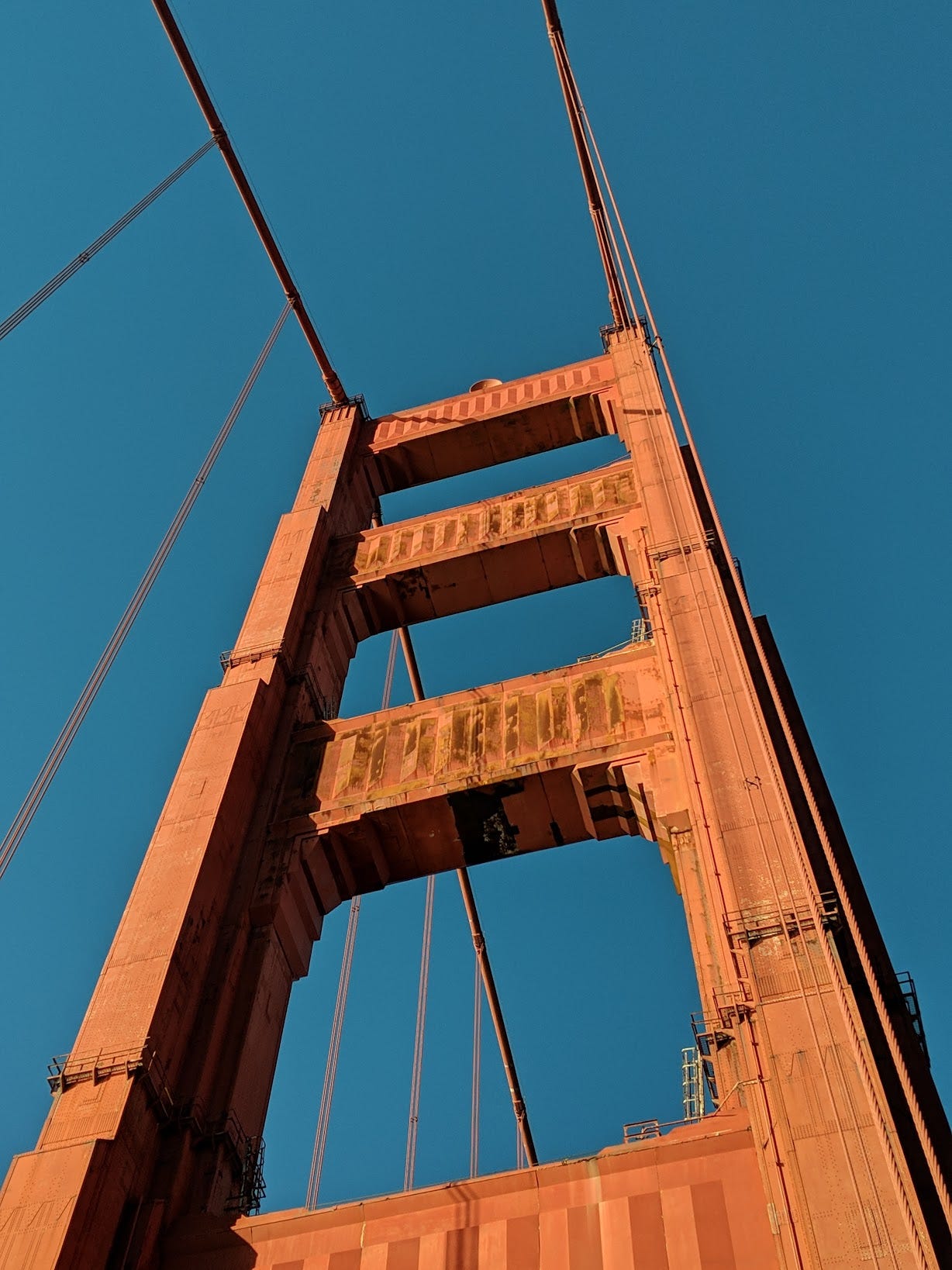 A tall red support of the Golden Gate Bridge stands below a dark blue sky, with large cables extending off it in two directions.