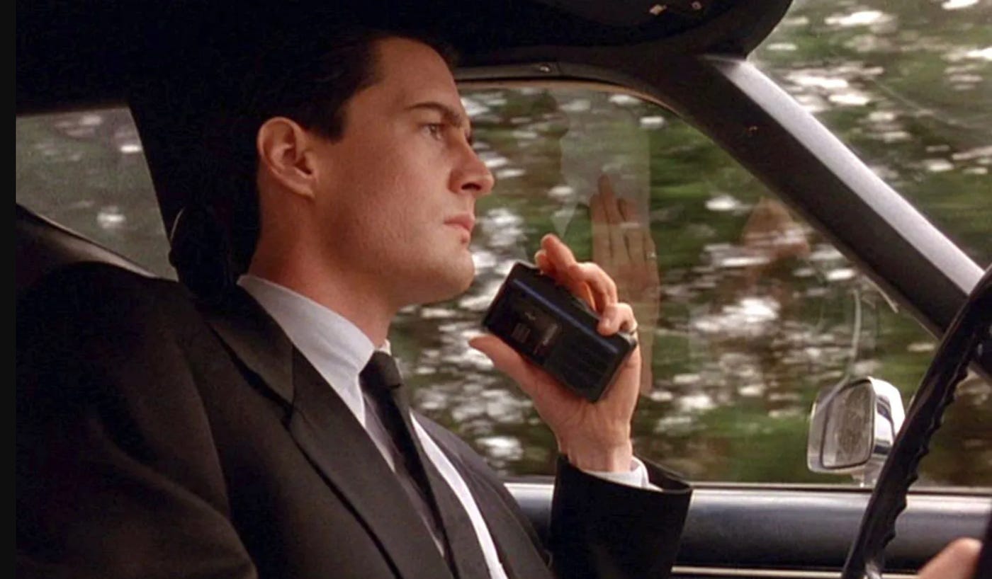 Actor Kyle McLachlan as Agent Dale Cooper in Twin Peaks, speaks into a dictaphone while driving his car.