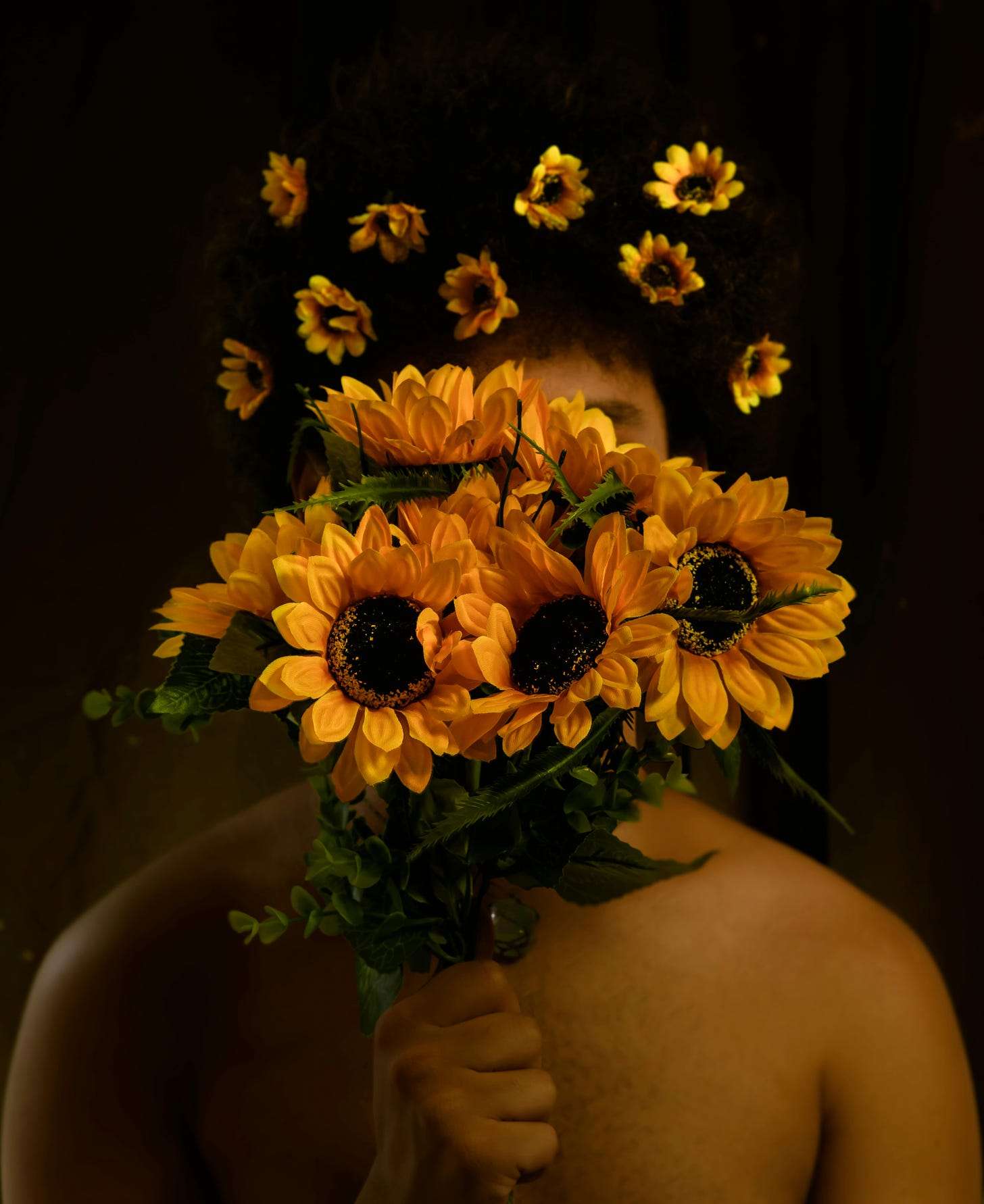 White man holding a bouquet of sunflowers in front of his face. There are also little sunflowers in his dark hair. 