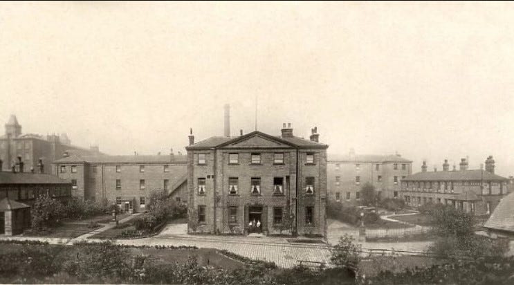 A sepia photograph of an austere, imposing three-storey building with further buildings in the background. 