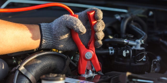 A gloved hand hooking up a jumper cable clamp to a car battery