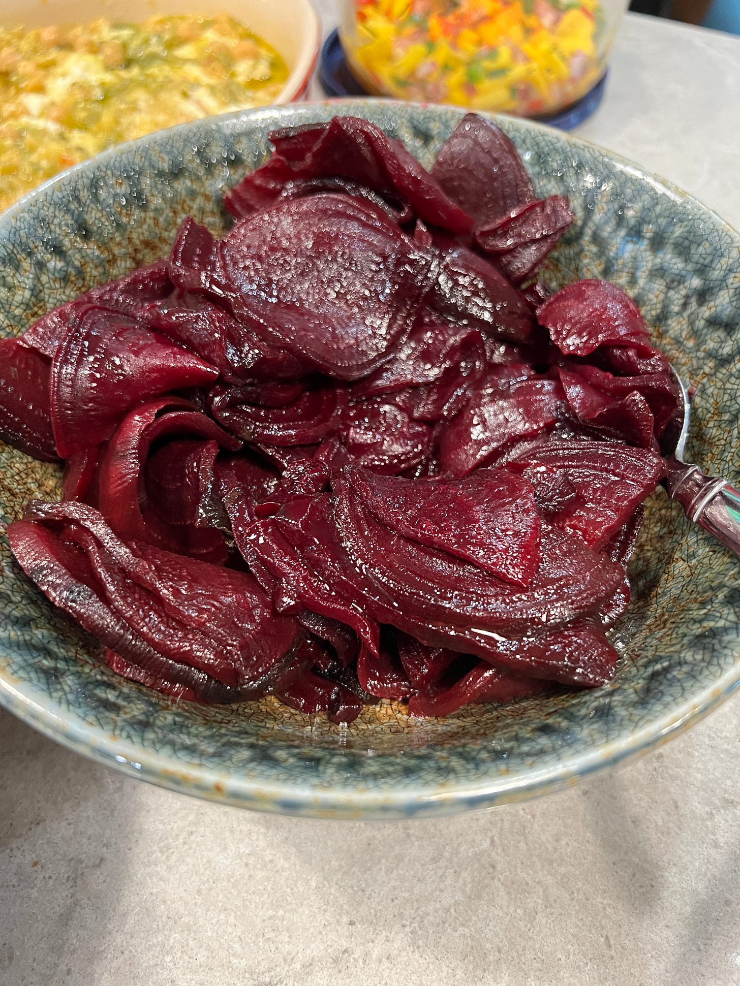 A blue pottery bowl filled with thin slices of deep red, roasted beets.