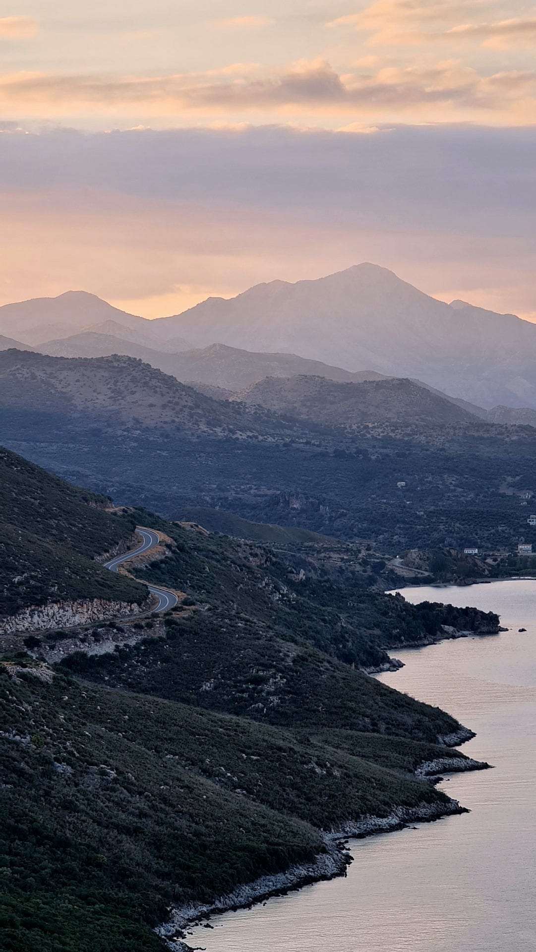 Tramonto su un paesaggio: mare e montagne, con una strada a curve che corre tra le rocce