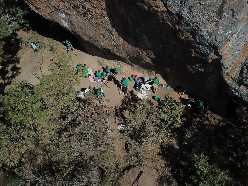 An overhead view of archaeologists working next to a high cliff face An overhead view of archaeologists working next to a high cliff face