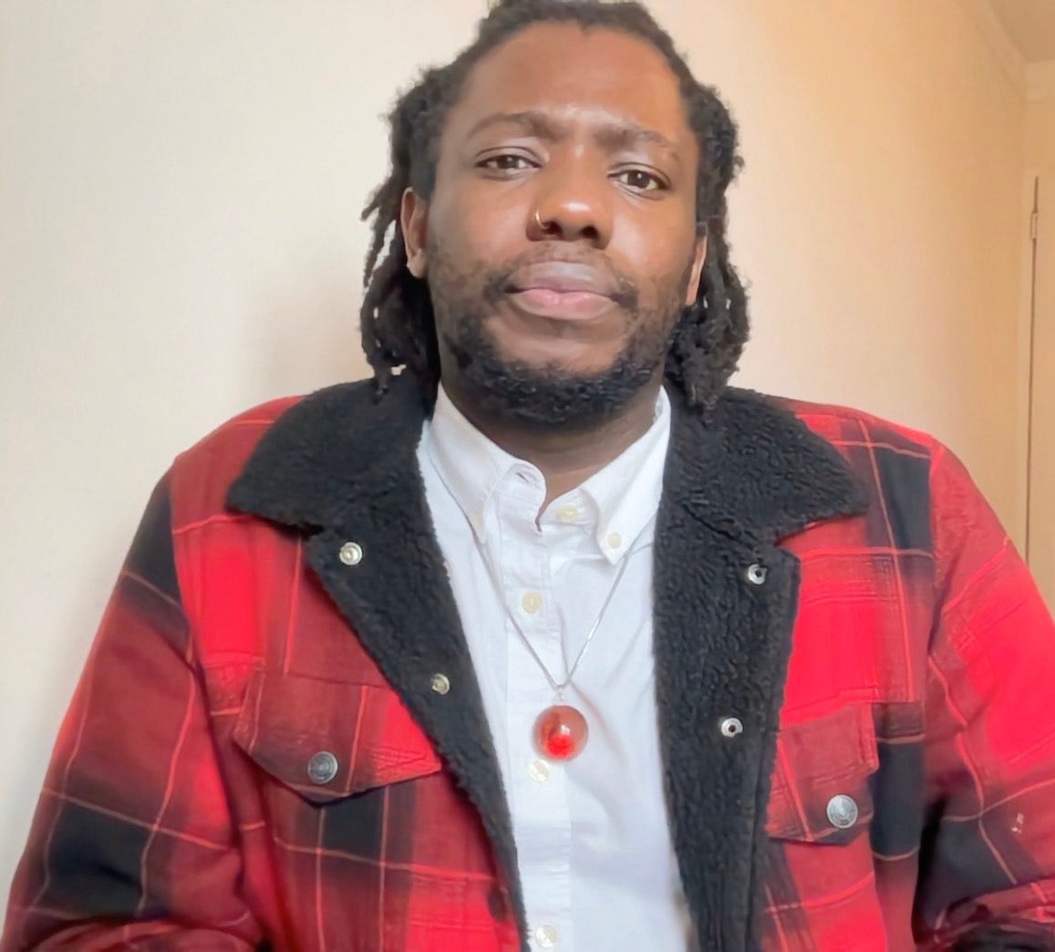 Zito Madu is the author of The Minotaur at Calla Lanza and here he looks at the camera in a white oxford shirt and a buffalo plaid jacket.