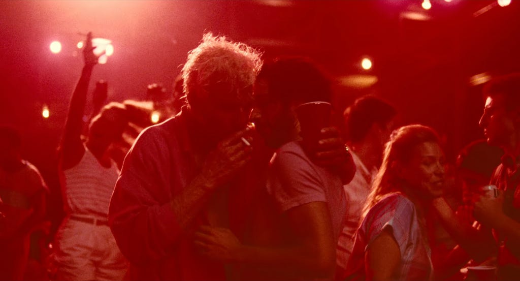 Movie still from Maestro. People dance and smoke together in a busy club.