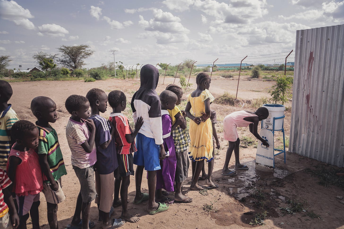 Black children in a line, waiting to get a ration of water in the Kakuma refugee camp.