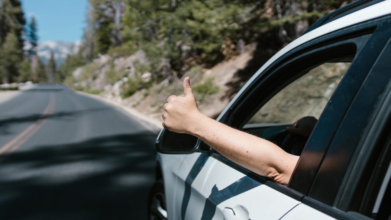 A person holding a thumbs up out the window of a vehicle. 