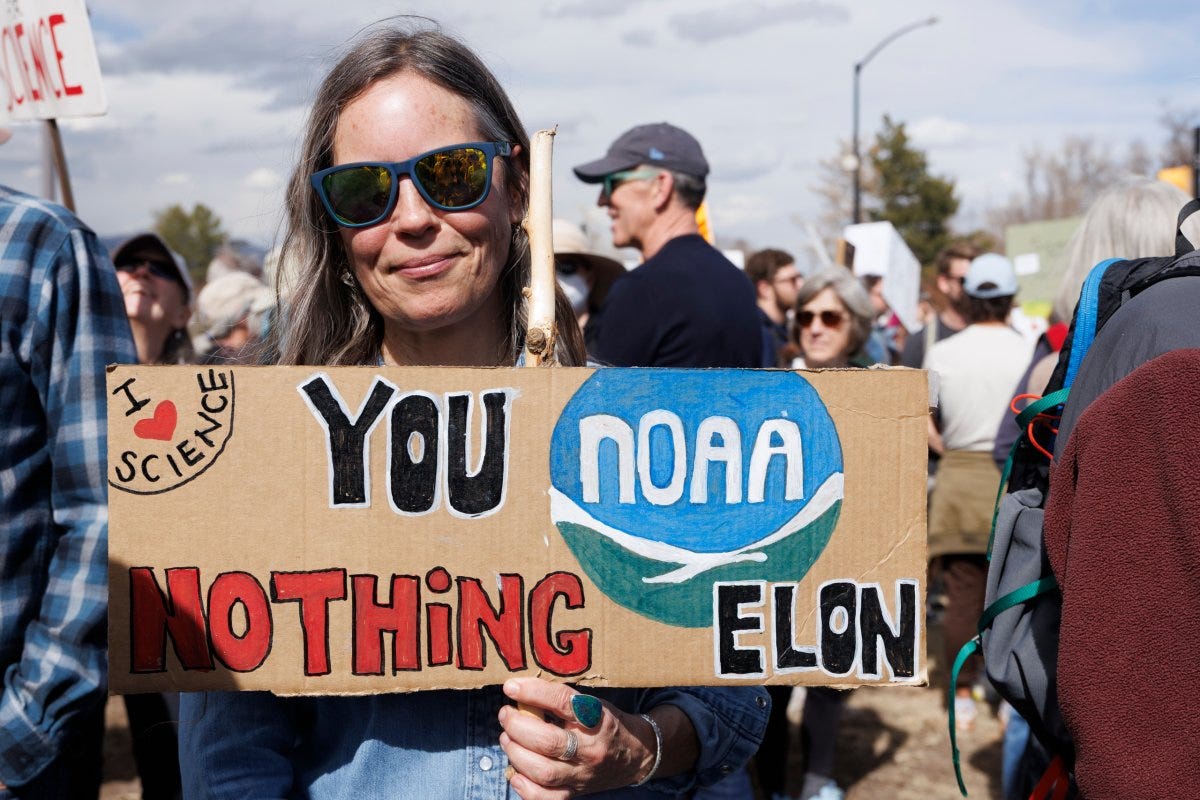 A woman holds up a hand-painted sign reading "You NOAA nothing Elon" during a protest outside the NOAA research station in Boulder A woman holds up a hand-painted sign reading "You NOAA nothing Elon" during a protest outside the NOAA research station in Boulder